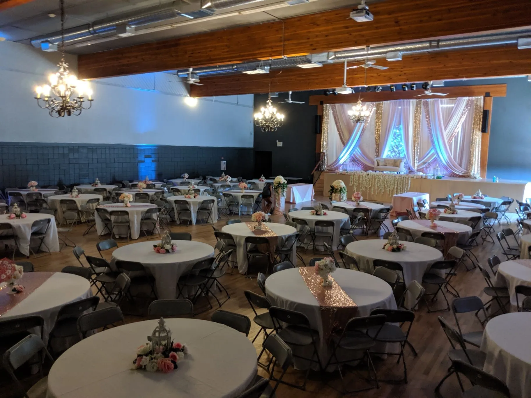 Rutland Centennial Hall set for a wedding reception, with round tables, chandeliers and a decorated stage